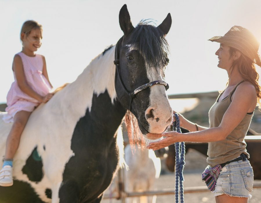 Little girl riding on horseback outdoor at ranch - Mother and daughter enjoy day together