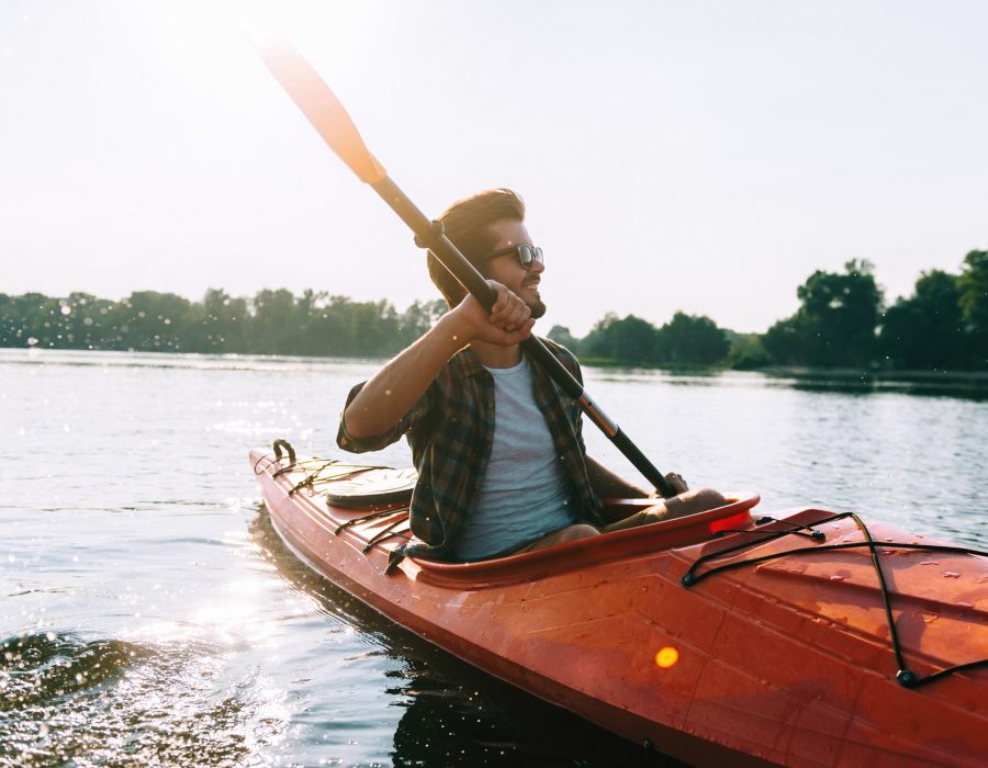 Man kayaking. Handsome young man kayaking on lake and smiling