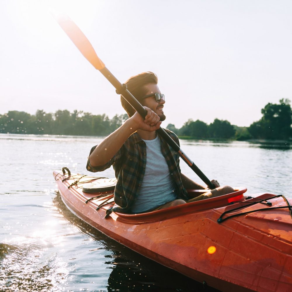 Man kayaking. Handsome young man kayaking on lake and smiling